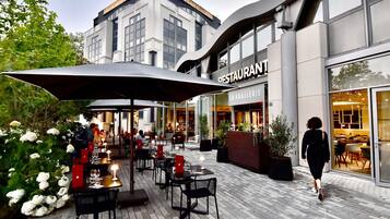 An outdoor dining area with tables and chairs, a large umbrella, and a building with a restaurant sign.