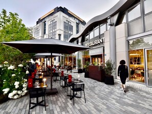 Un área de comedor al aire libre con mesas y sillas, un paraguas grande y un edificio con letrero de restaurante.