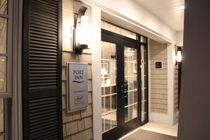 A hotel entrance with a sign for 'Port Inn,' a black door, and a light fixture above the door. - Port Inn & Suites Kennebunk, an Ascend Collection Hotel (Kennebunk)