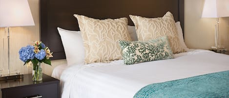 Ein Hotelzimmer mit einem großen Bett, zwei Nachttischen und einem Beistelltisch mit Blumen in einer Vase.