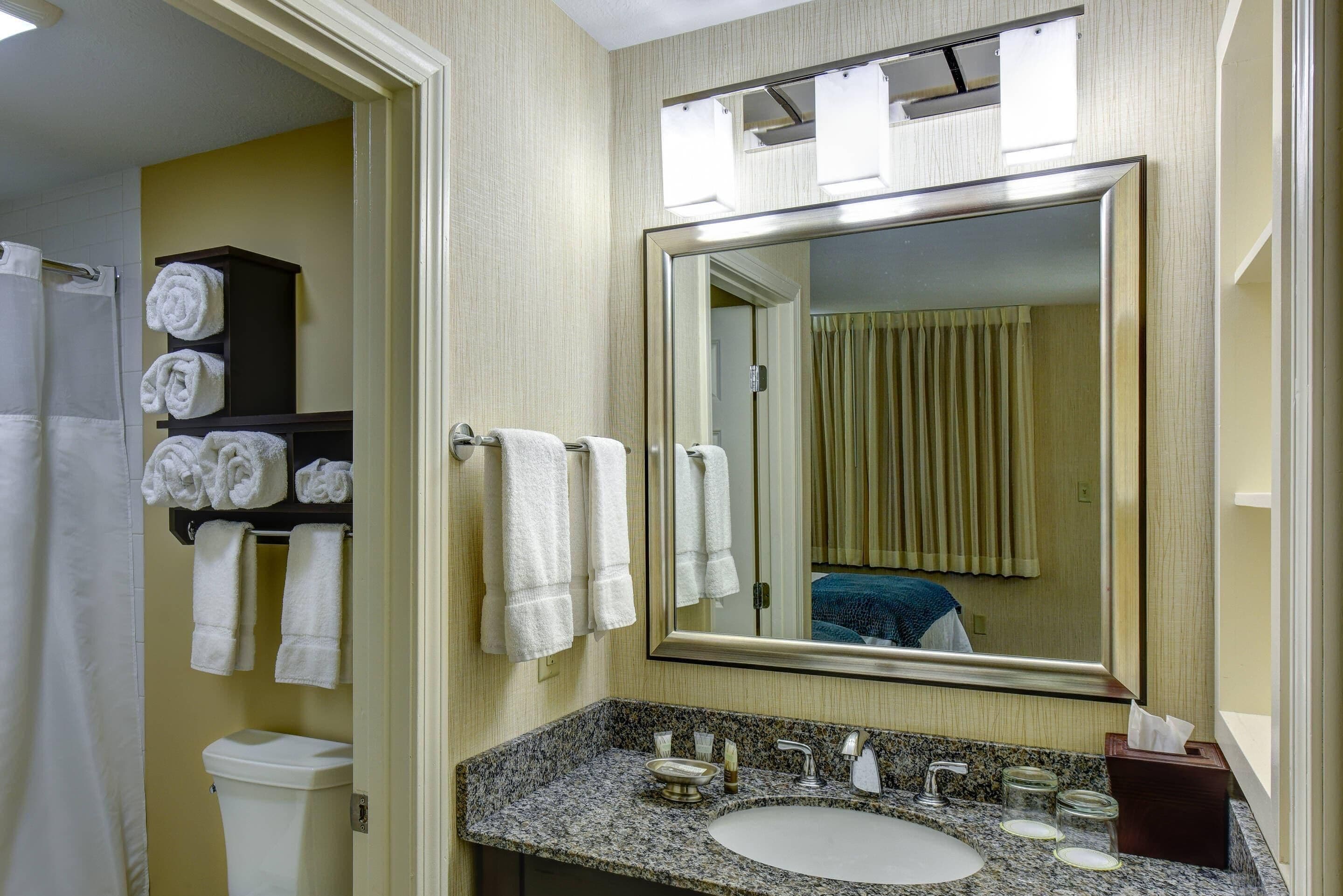 A bathroom with a sink, mirror, towels, and a toilet.