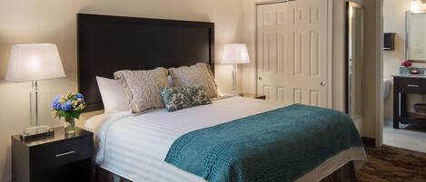 A hotel room with a large bed, two bedside tables, a nightstand, a mirror, and a door.