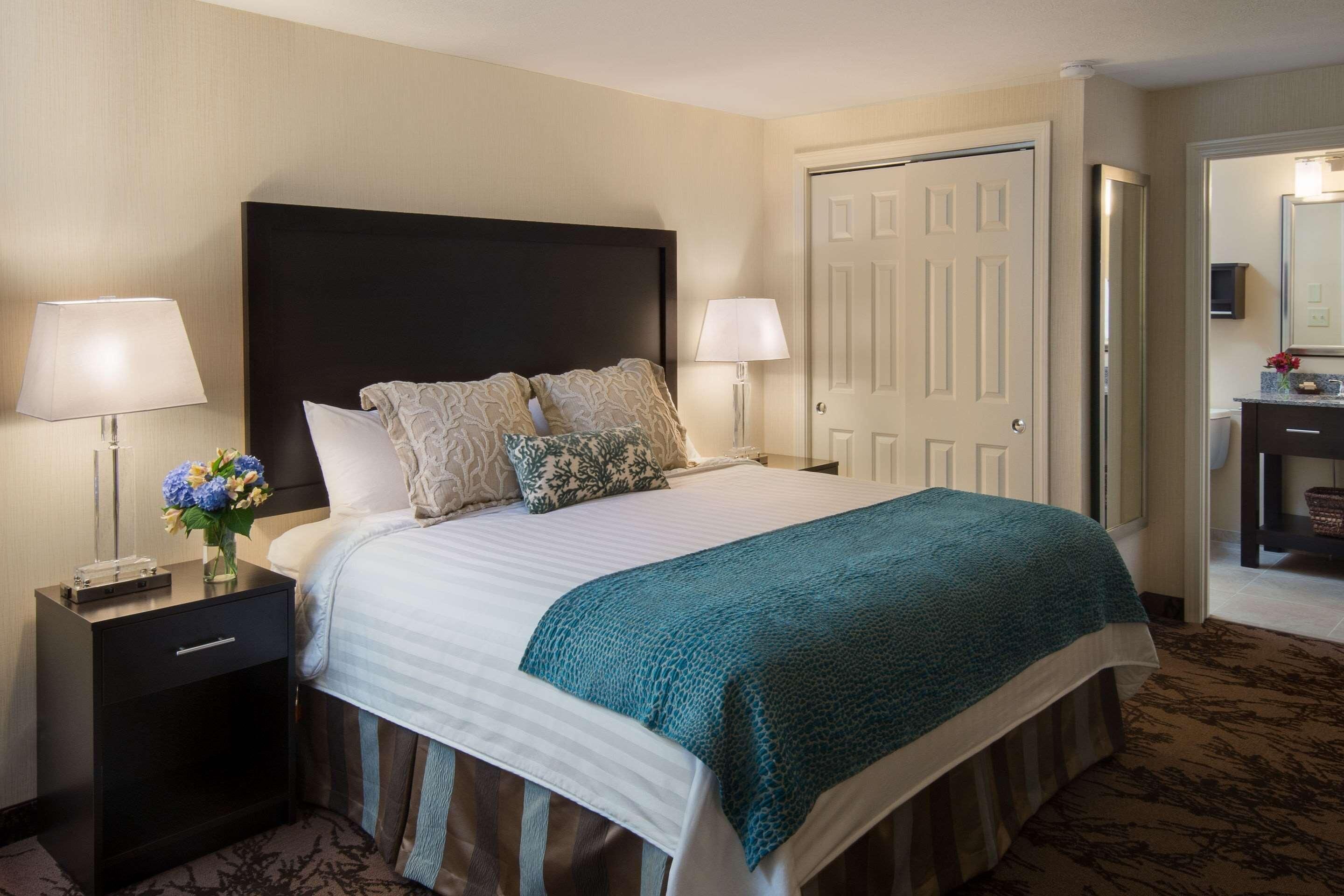 A hotel room with a bed, two bedside lamps, a nightstand, a dresser, and a door.