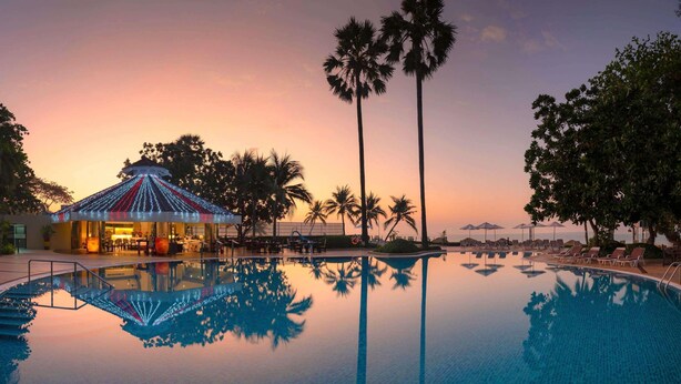 A poolside area with a lounge, palm trees, and a sunset. - Novotel Rayong Rim Pae Resort (Klaeng)