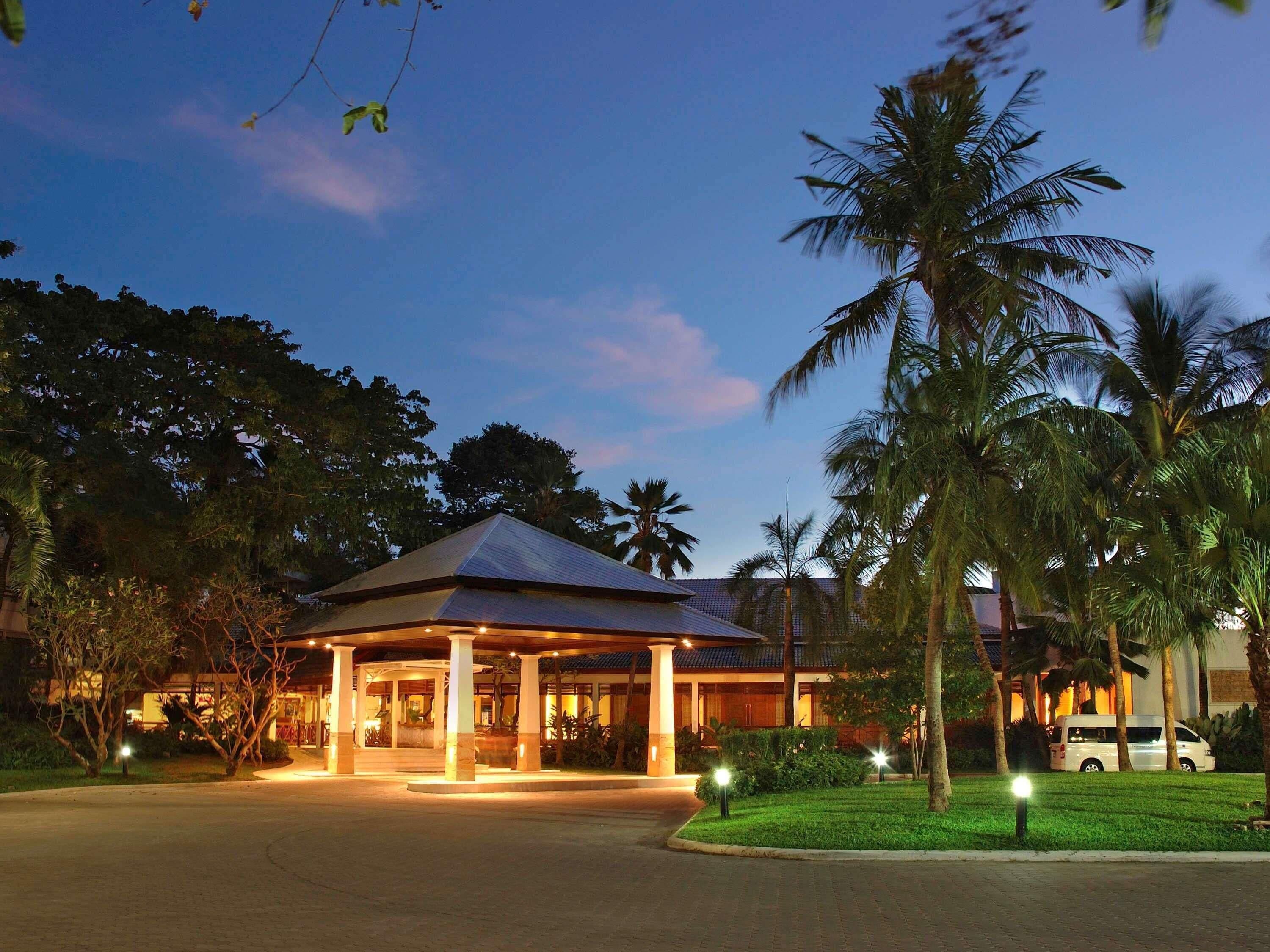 A hotel entrance with a covered walkway, palm trees, and a vehicle parked nearby.