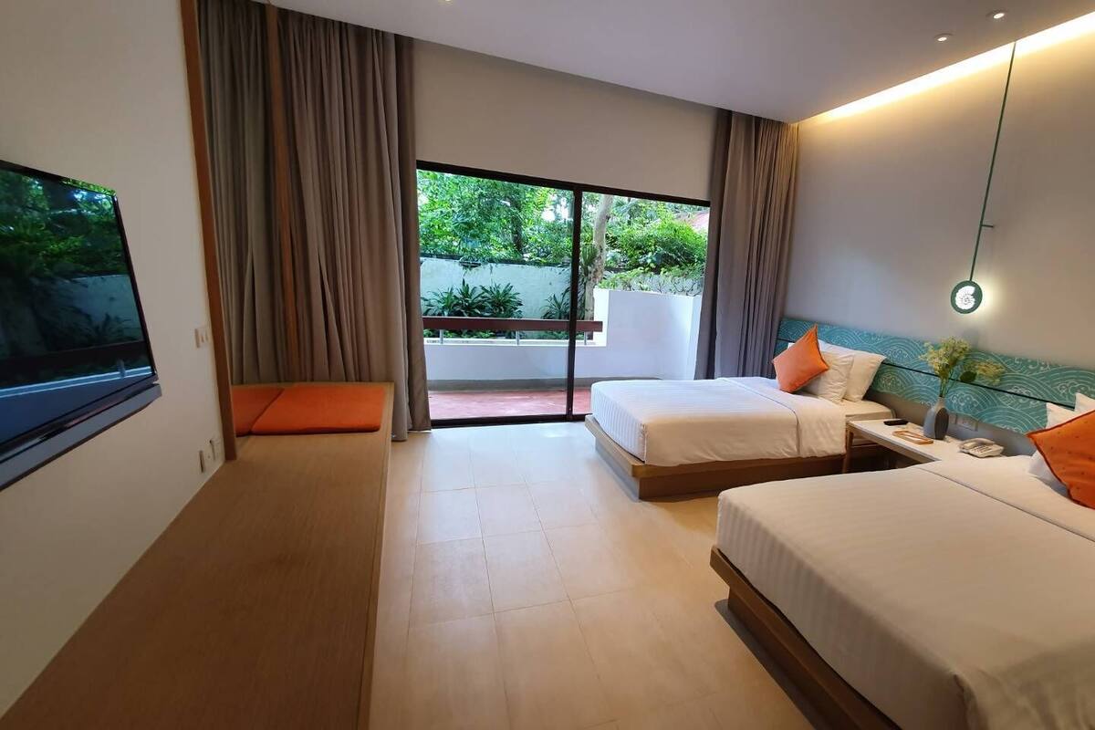 Habitación de hotel con dos camas, un ventanal grande y vistas a zonas verdes.