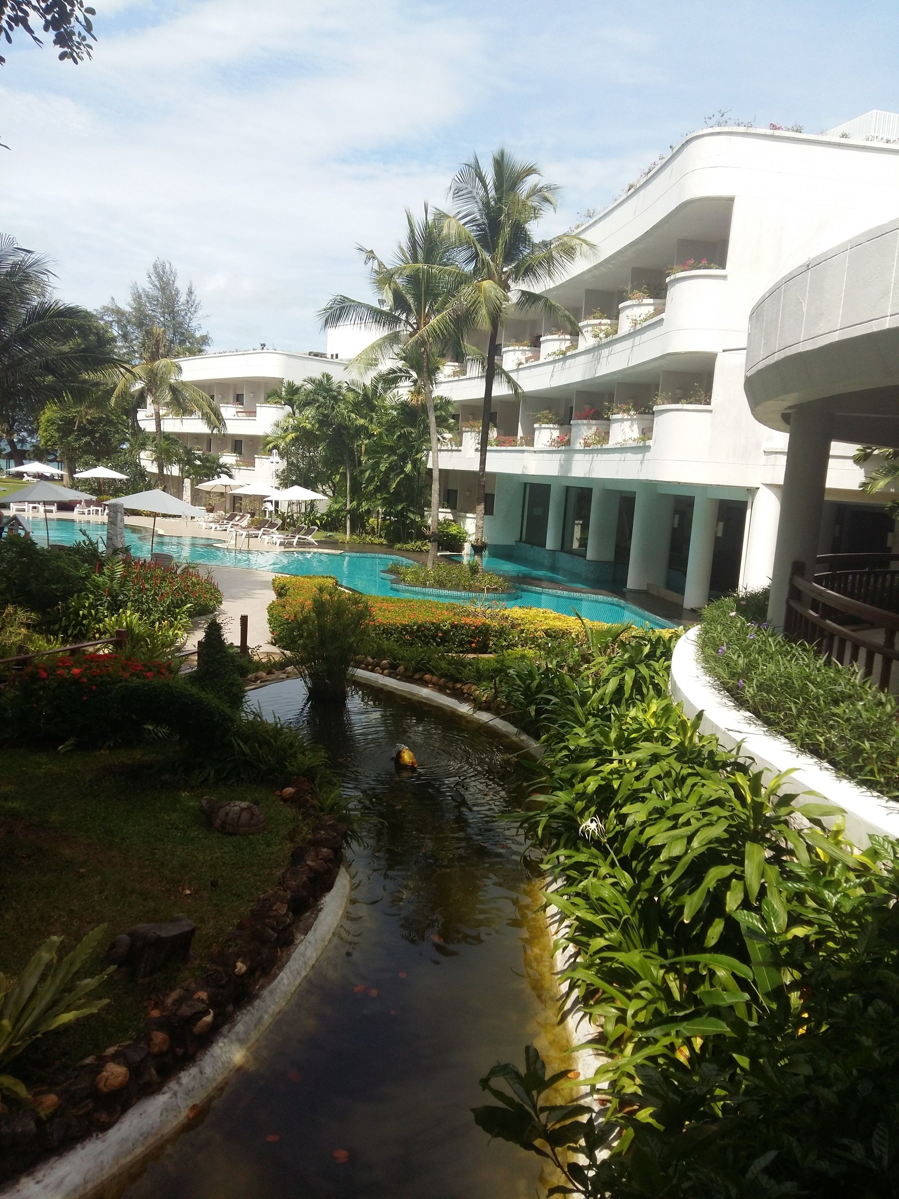 A resort with a swimming pool, palm trees, and a small water feature.