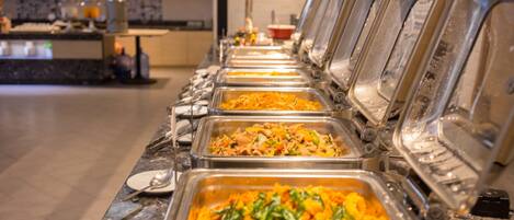 A buffet line with various dishes, including a dish with orange-colored food and green garnish, in a well-lit indoor setting.