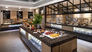 A modern breakfast buffet with a variety of food options, a large potted plant, and decorative ceiling artwork. - Novotel Rayong Rim Pae Resort (Klaeng)