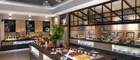 A modern breakfast buffet with a variety of food options, a large potted plant, and decorative ceiling artwork.