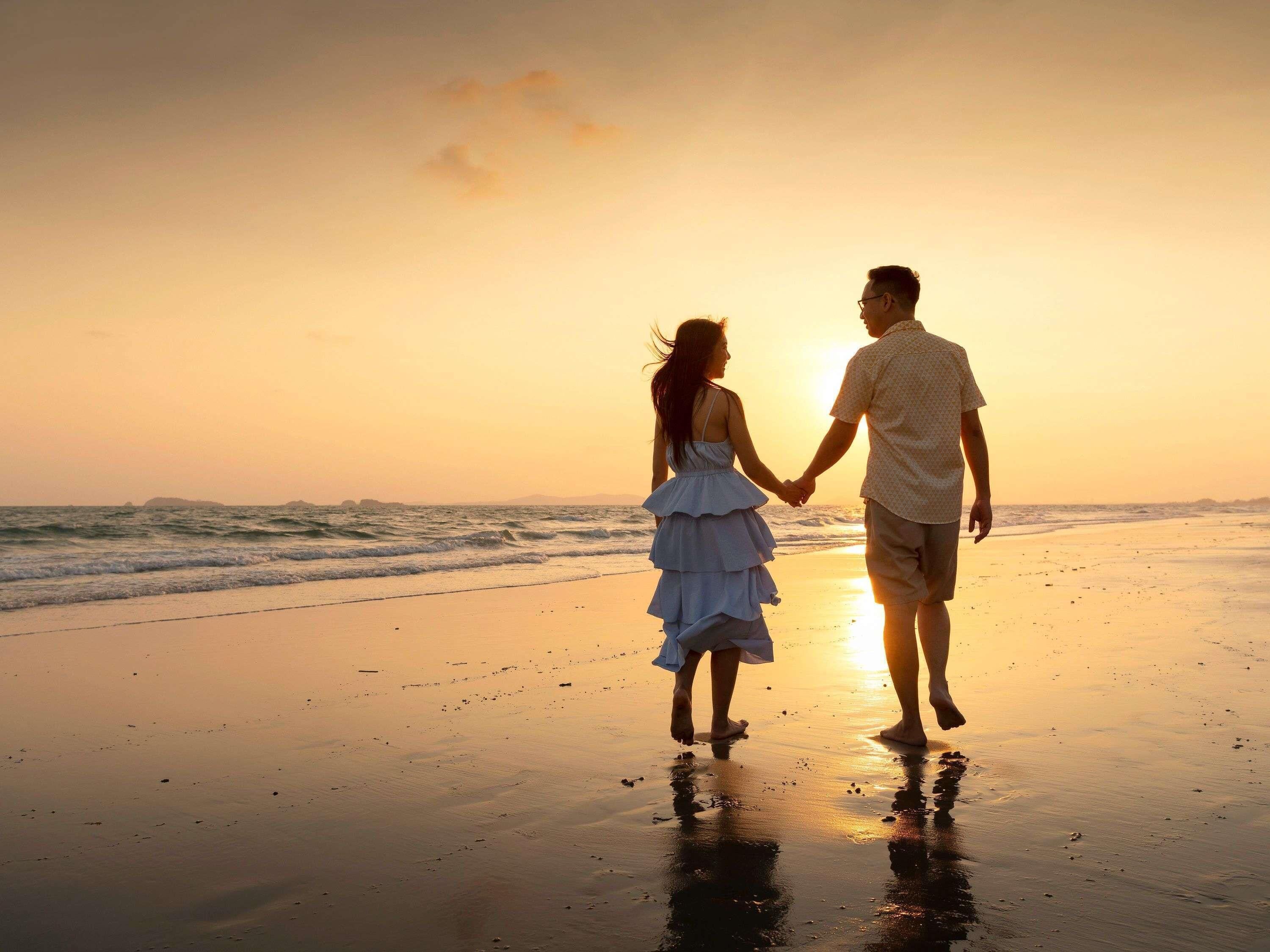 Una pareja caminando por la playa al atardecer.