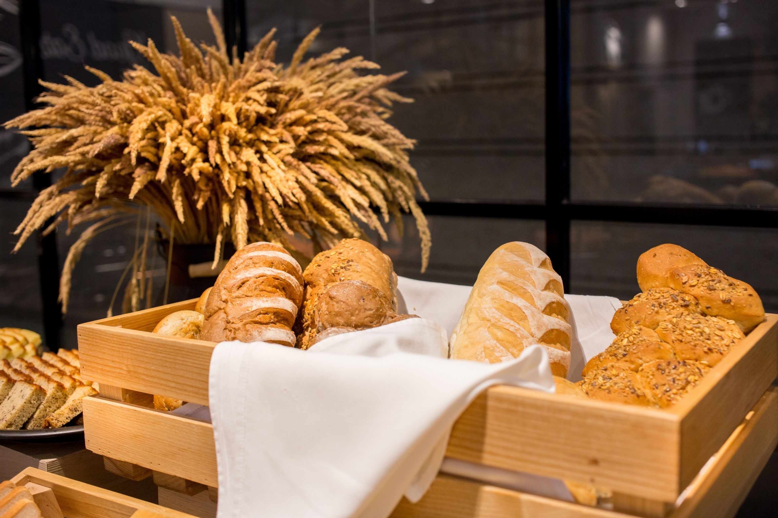 A wooden bread basket filled with various types of bread, including baguettes and rolls, placed on a table.