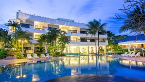 A hotel with a swimming pool, lounge chairs, and a well-lit outdoor area.