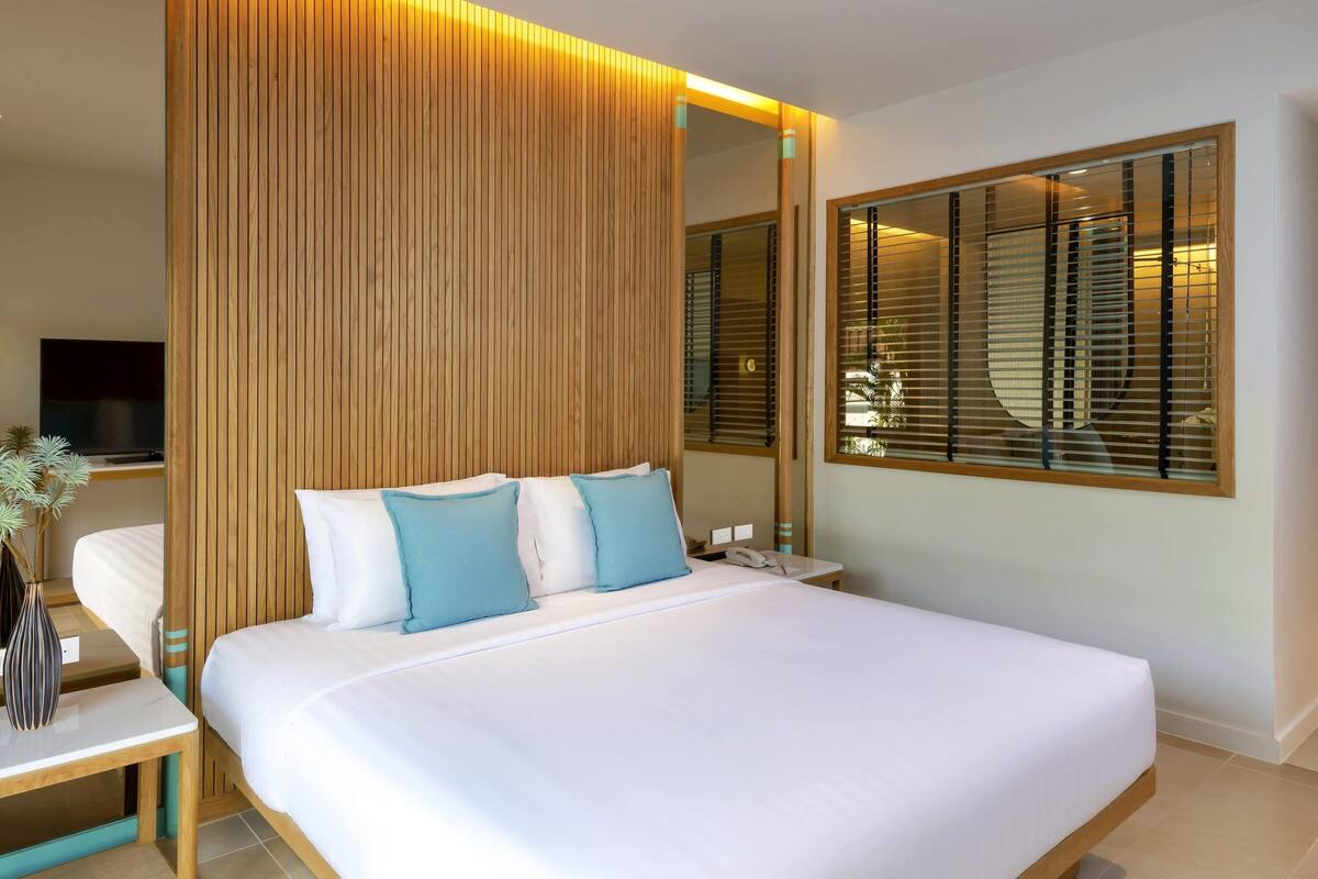Una habitación de hotel moderna con una cama grande, un panel de pared de madera y un ventanal con persianas.