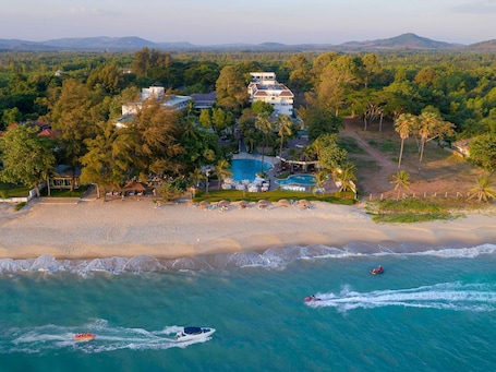An aerial view of a resort with a large pool, beachfront, and boats in the water.. Novotel Rayong Rim Pae Resort