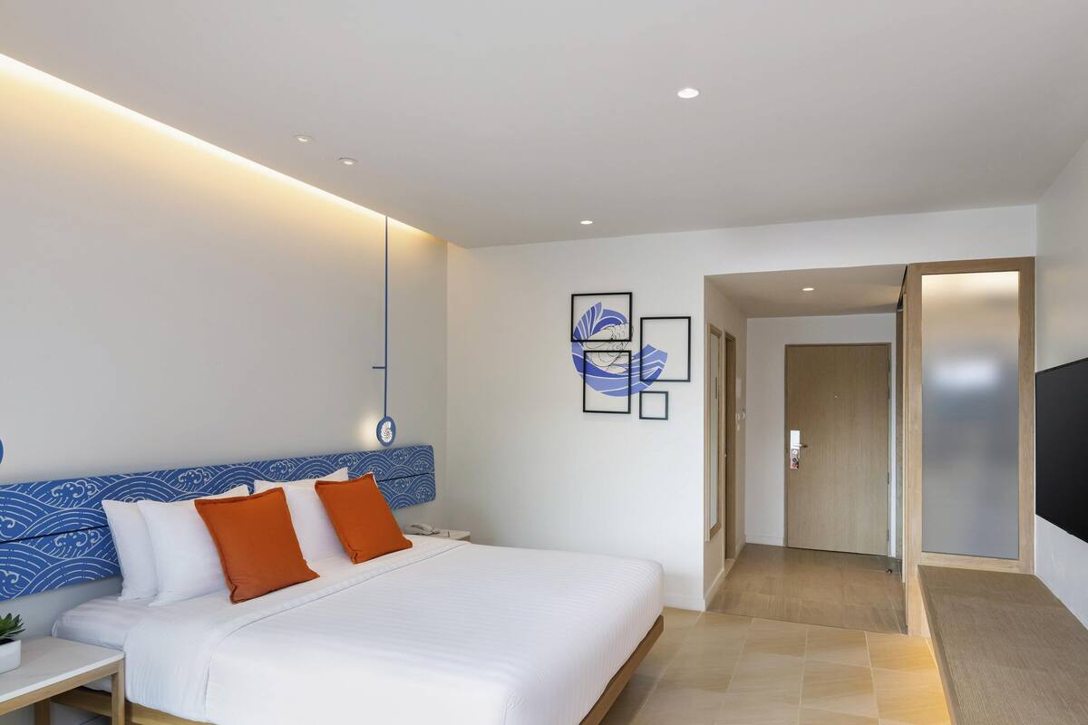 Habitación de hotel moderna con una cama grande, una mesita de noche, un teléfono en la pared y un televisor de pantalla plana.