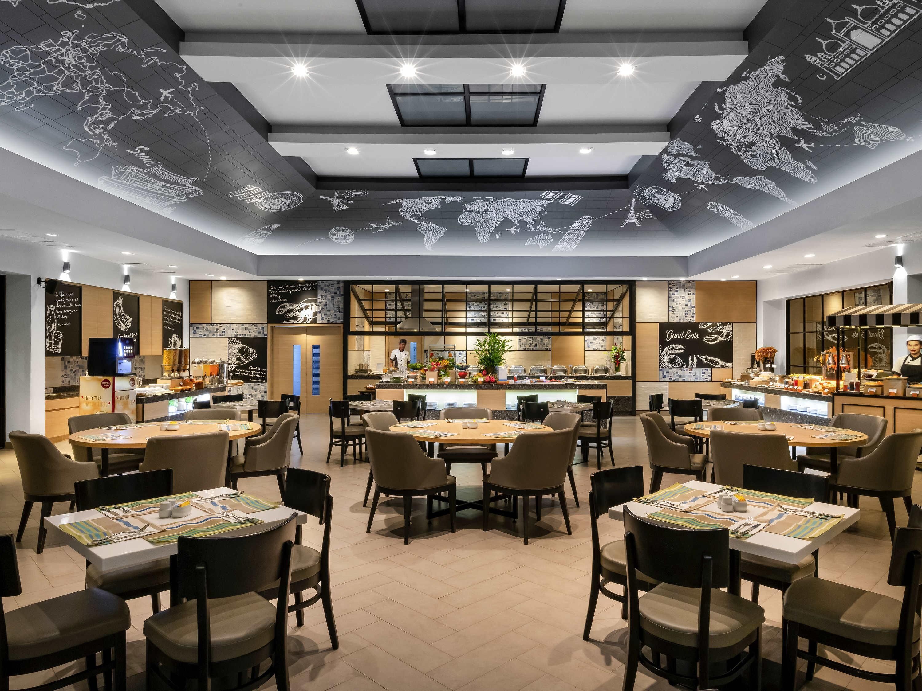 A restaurant with multiple dining tables, chairs, a kitchen area, and a world map on the ceiling.