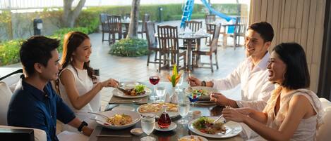 Un grupo de personas cenando en un restaurante al aire libre con una piscina y toboganes al fondo.