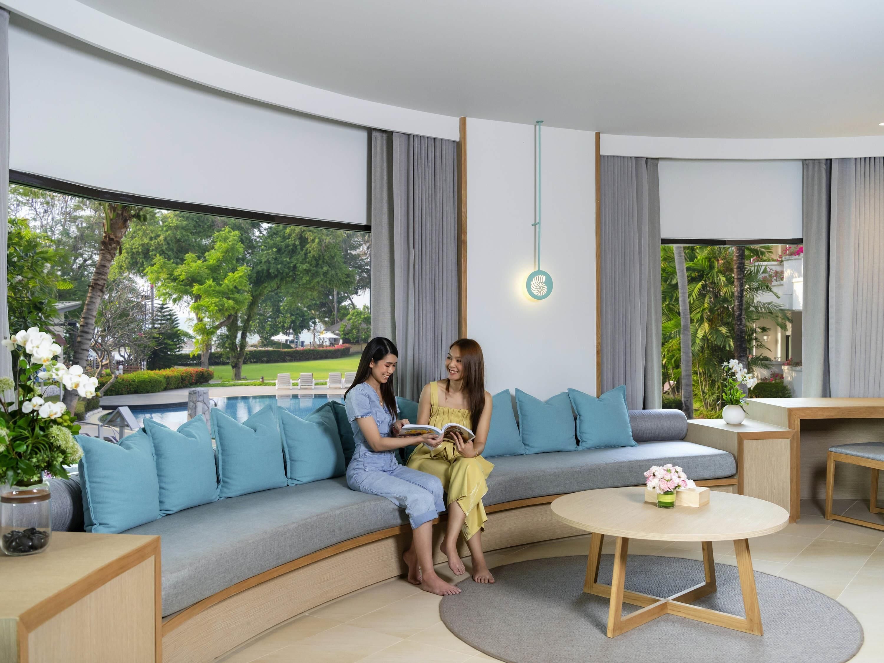 Un salón moderno con un sofá curvo, una mesa de centro redonda y vistas a una piscina y vegetación.