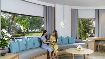 Un salón moderno con un sofá curvo, una mesa de centro redonda y vistas a una piscina y vegetación.