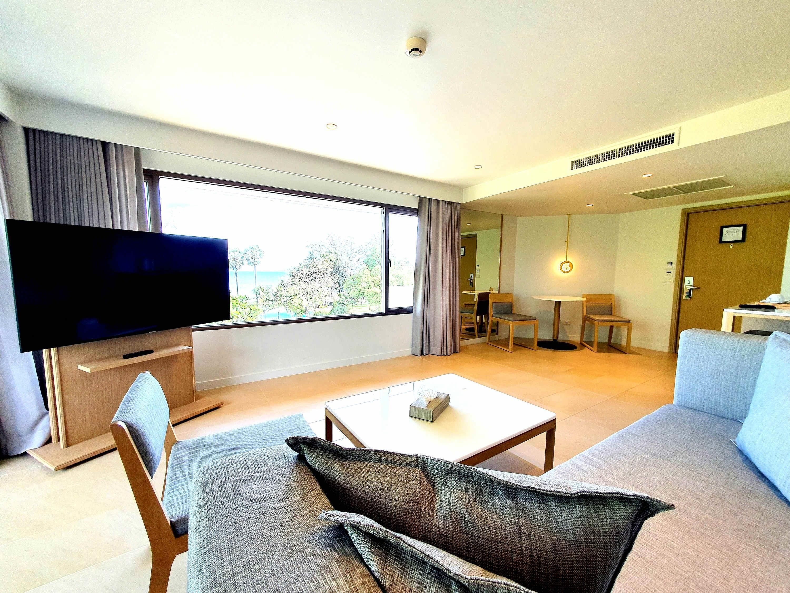 A modern living room with a flat-screen TV, a sofa, a coffee table, and a dining area with chairs and a table.