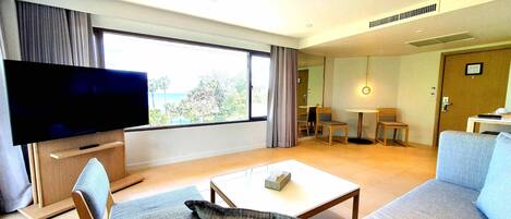 A modern living room with a flat-screen TV, a sofa, a coffee table, and a dining area with chairs and a table.