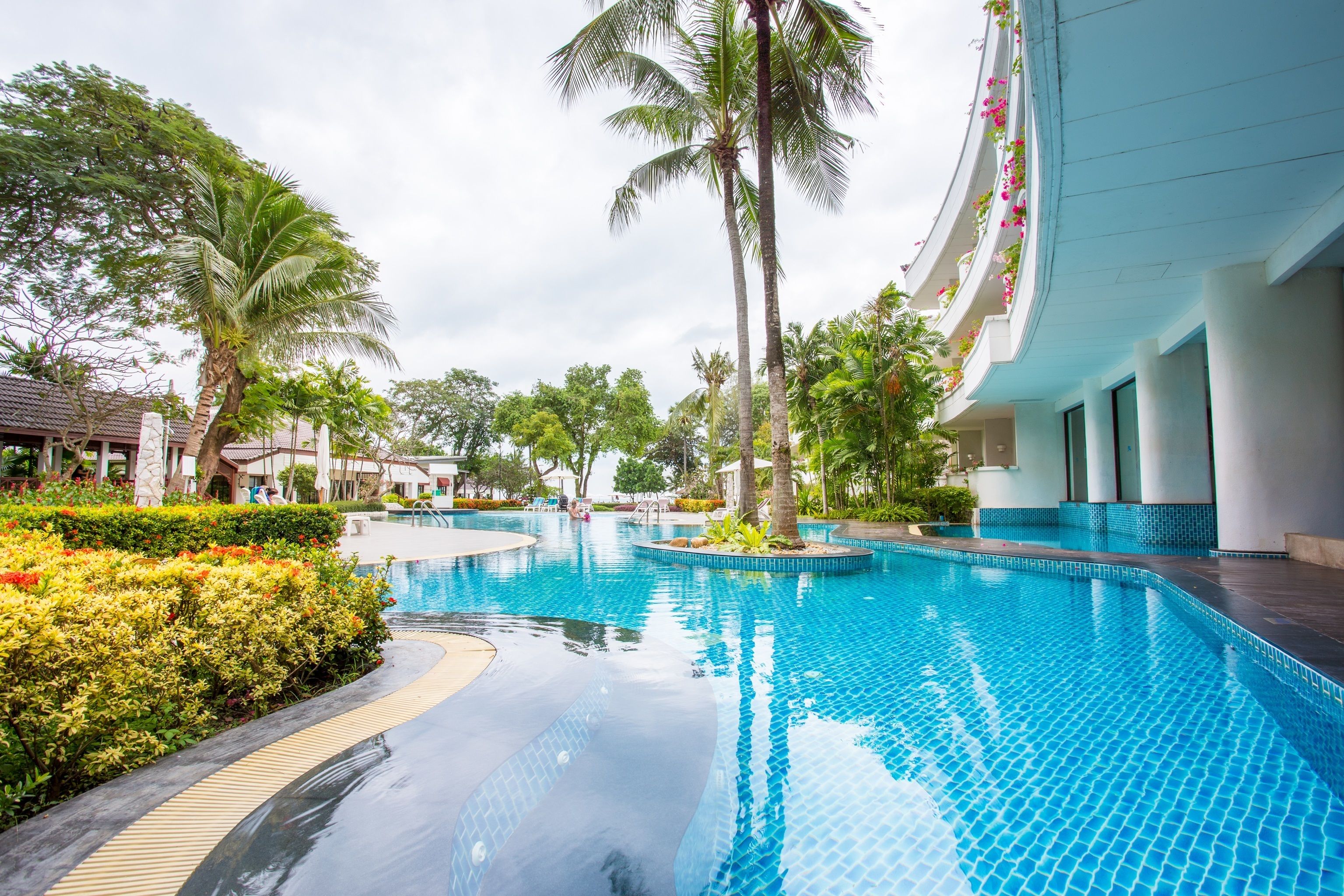 A swimming pool with tiled edges, surrounded by lush greenery and palm trees.