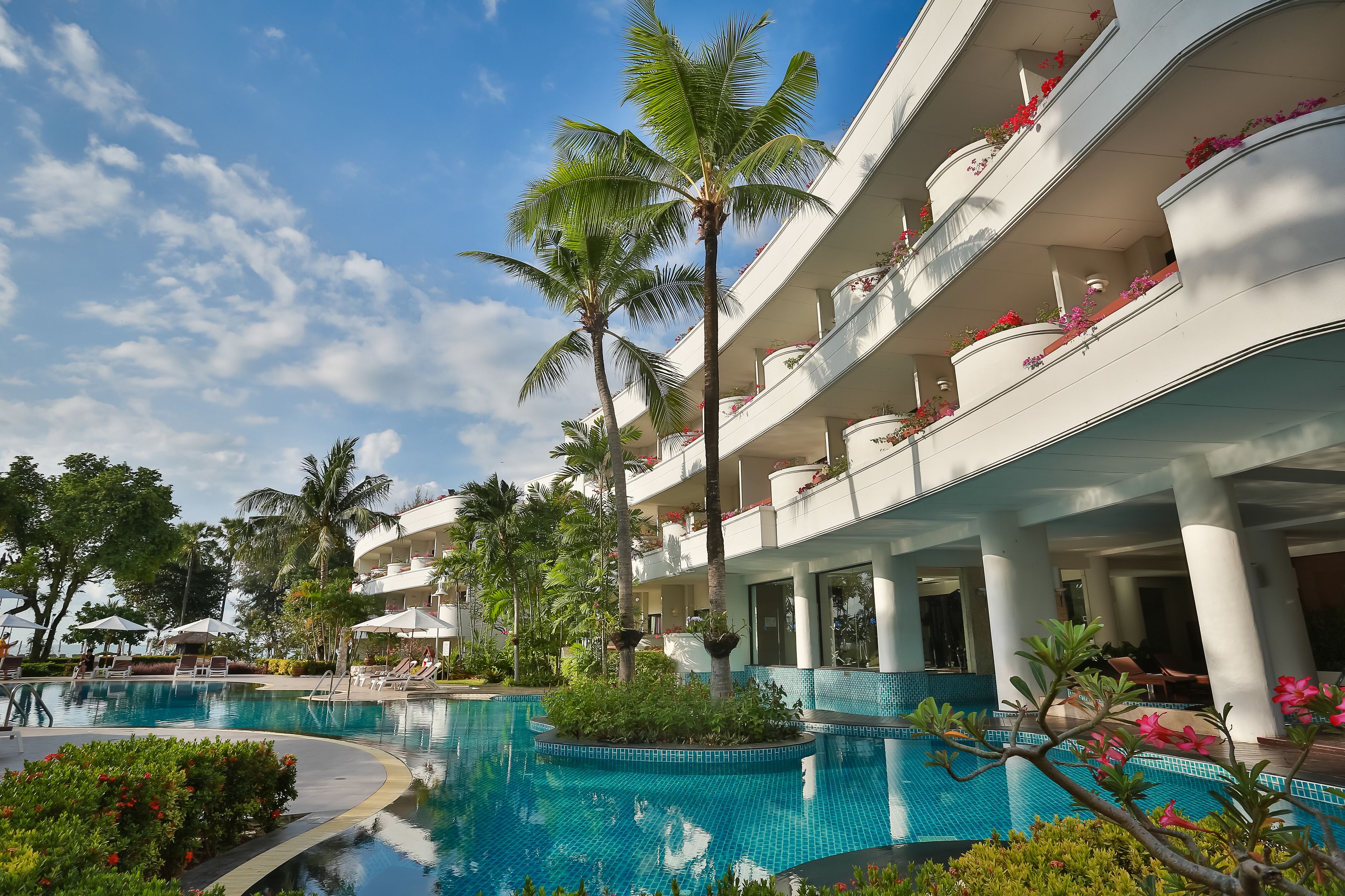 Ein Hotel mit Schwimmbad, Palmen und Balkonen mit Blumen.