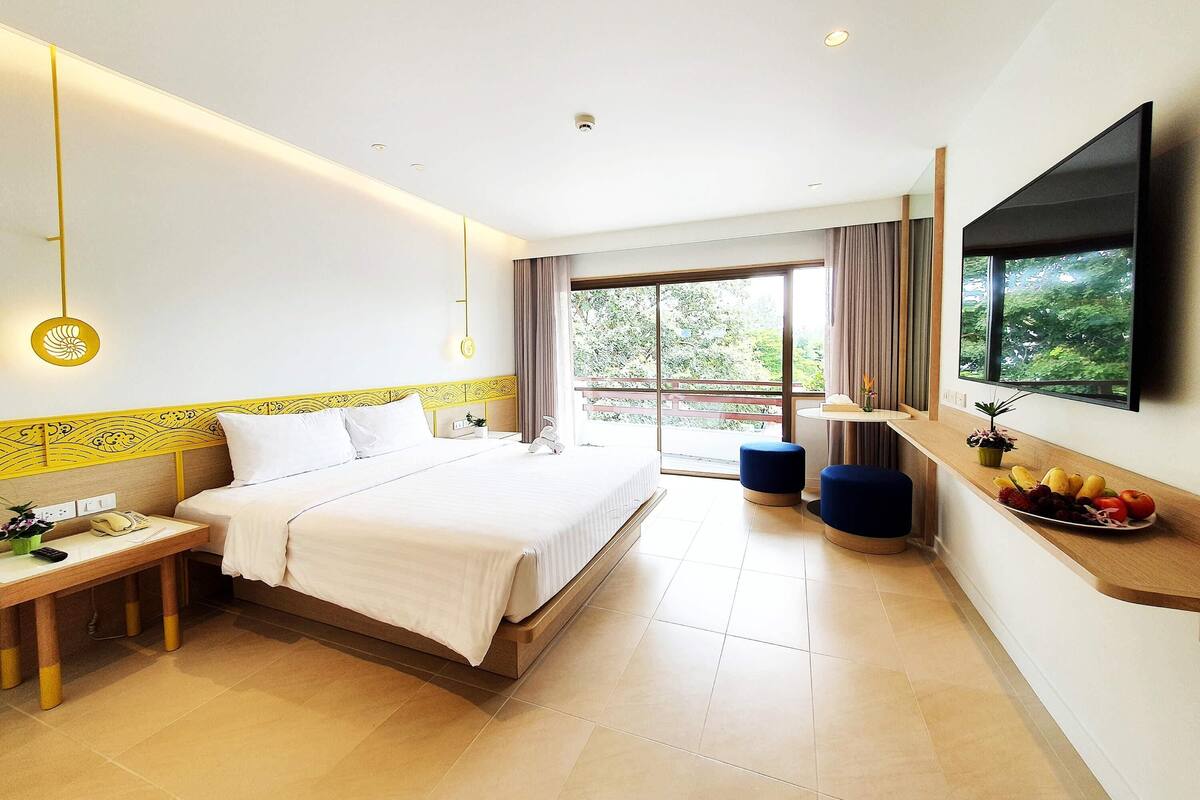 Habitación de hotel con cama, mesita de noche y un ventanal con vistas a zonas verdes.