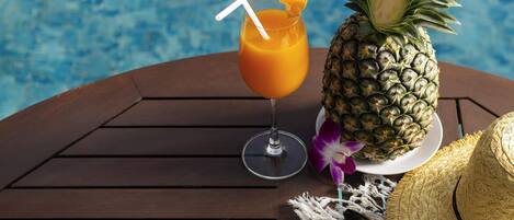 Cenário tropical com mesa de madeira junto a uma piscina, apresentando uma abacaxi, uma bebida com canudo, óculos de sol e um chapéu de palha.
