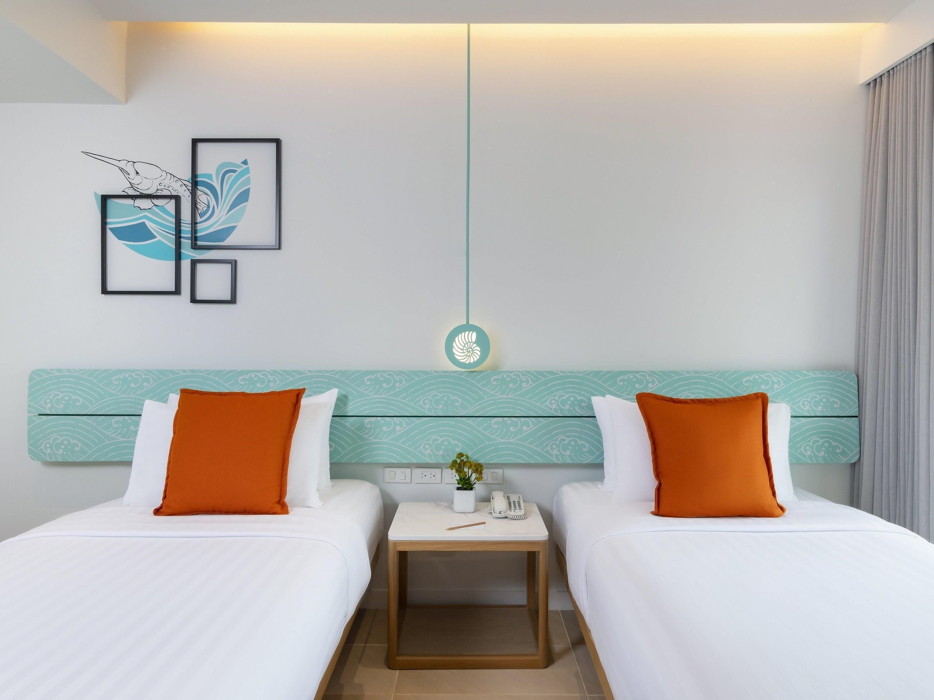 A hotel room with two beds, a nightstand, a wall-mounted light, and framed artwork.
