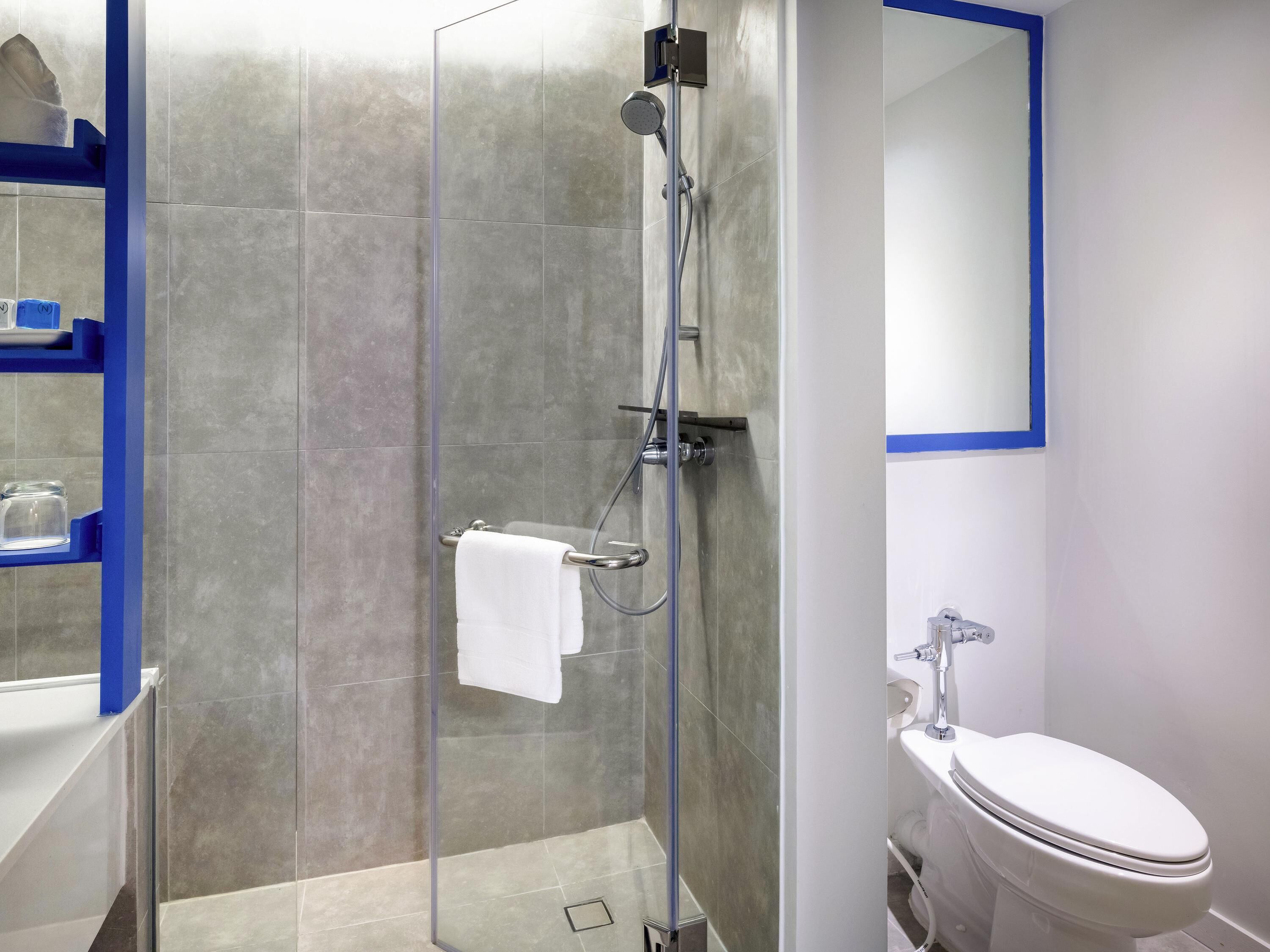 Et moderne badeværelse med bruseniche, et hvidt toilet og et spejl med blå ramme.