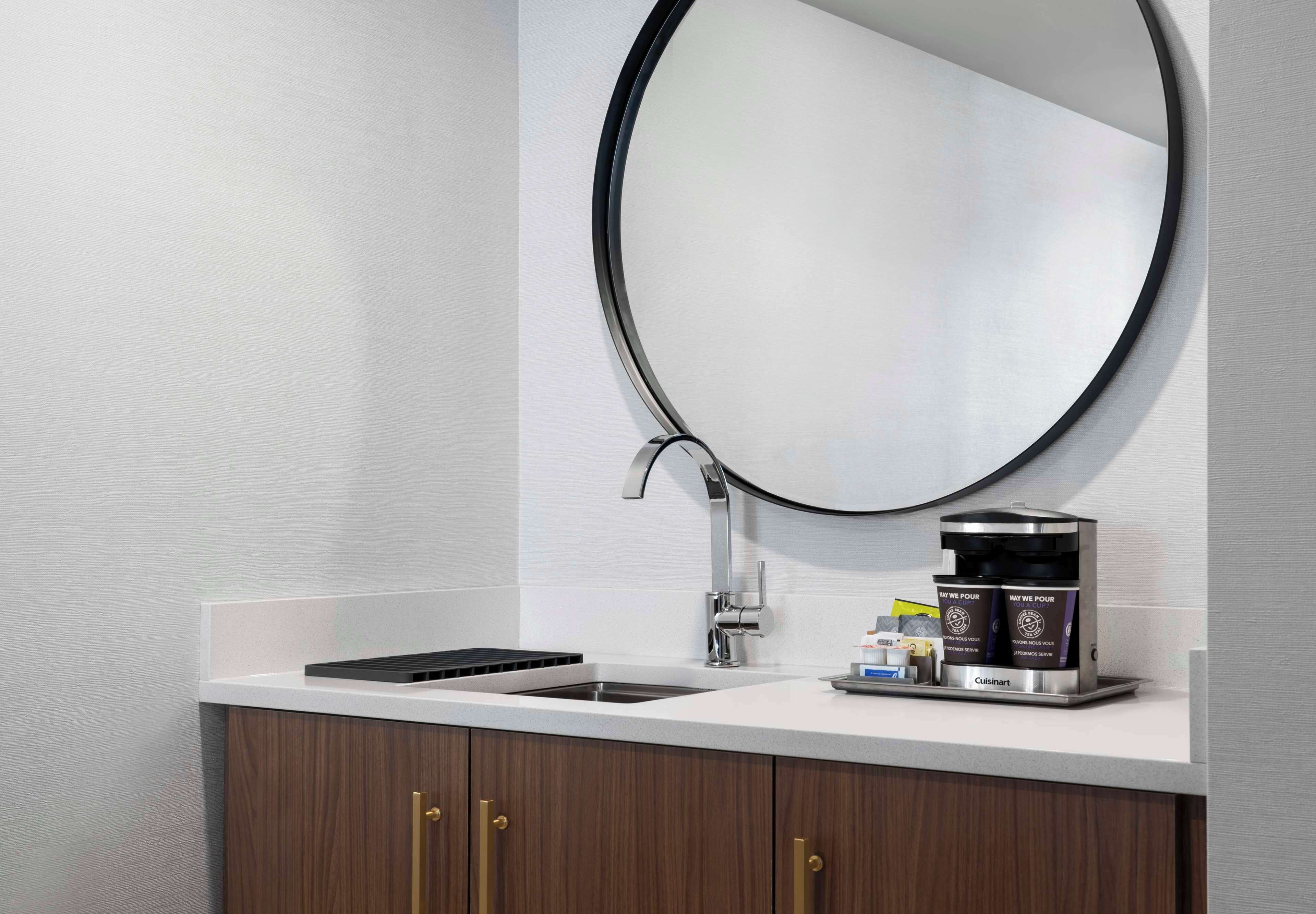 A modern bathroom with a white countertop, a sink, a mirror, and a coffee machine.