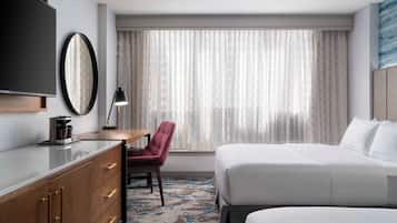 Habitació d'hotel amb un llit, escriptori amb cadira, televisió i finestra amb cortines.