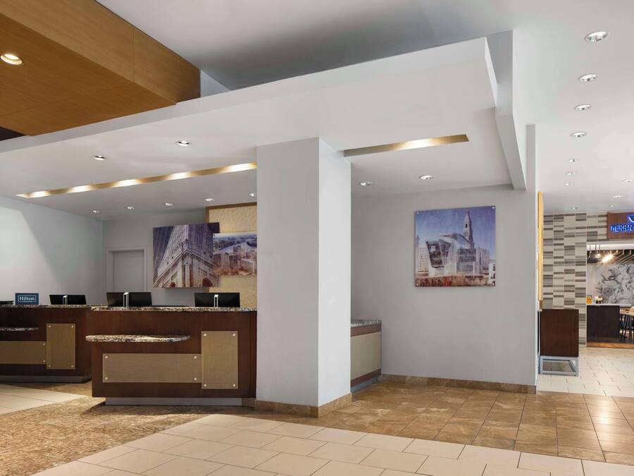 A hotel reception area with a modern design, featuring a reception desk, a digital display, and a seating area with a view of the cityscape.