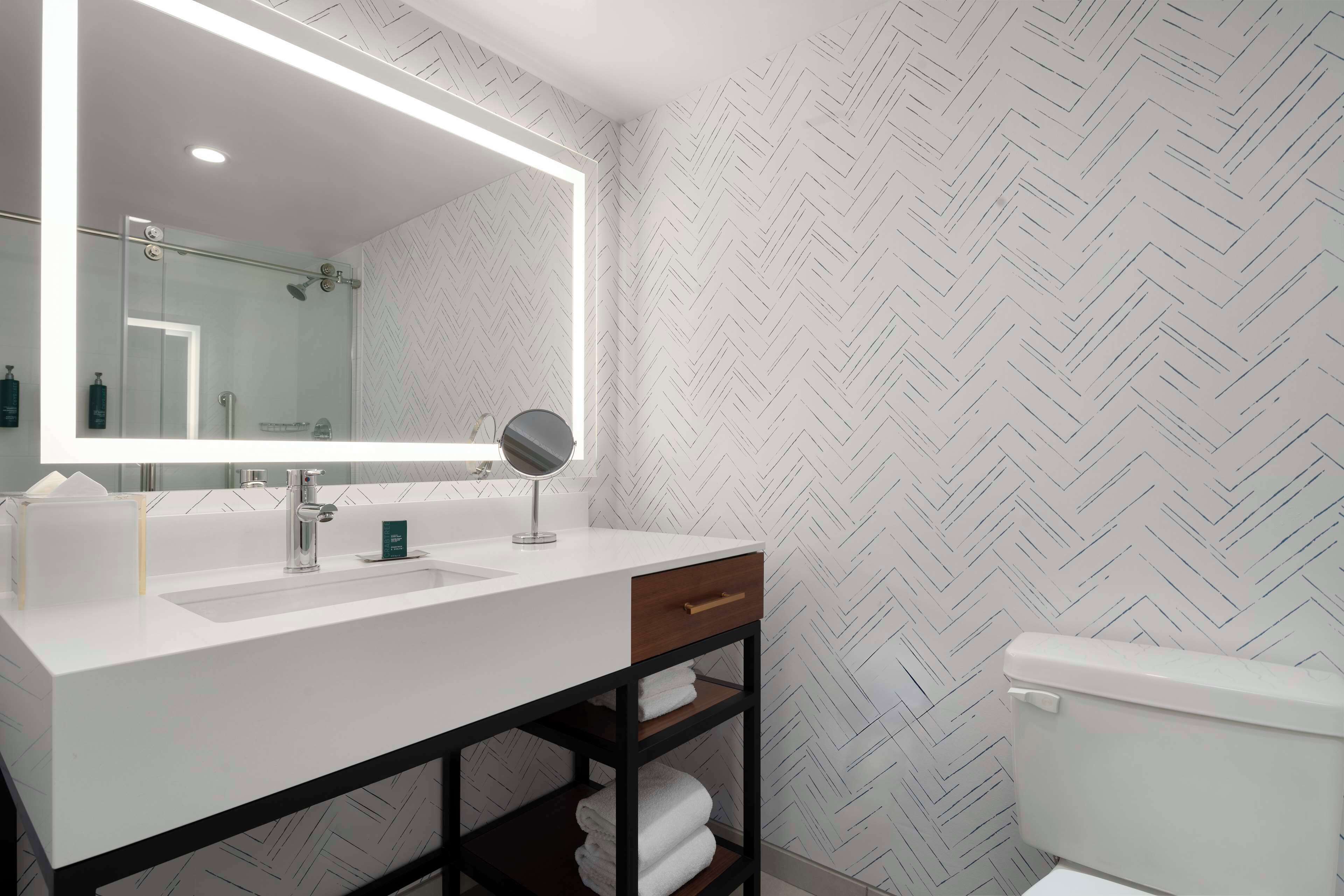 Ein modernes Badezimmer mit einem großen Spiegel, einem weißen Waschbecken und einer Toilette.