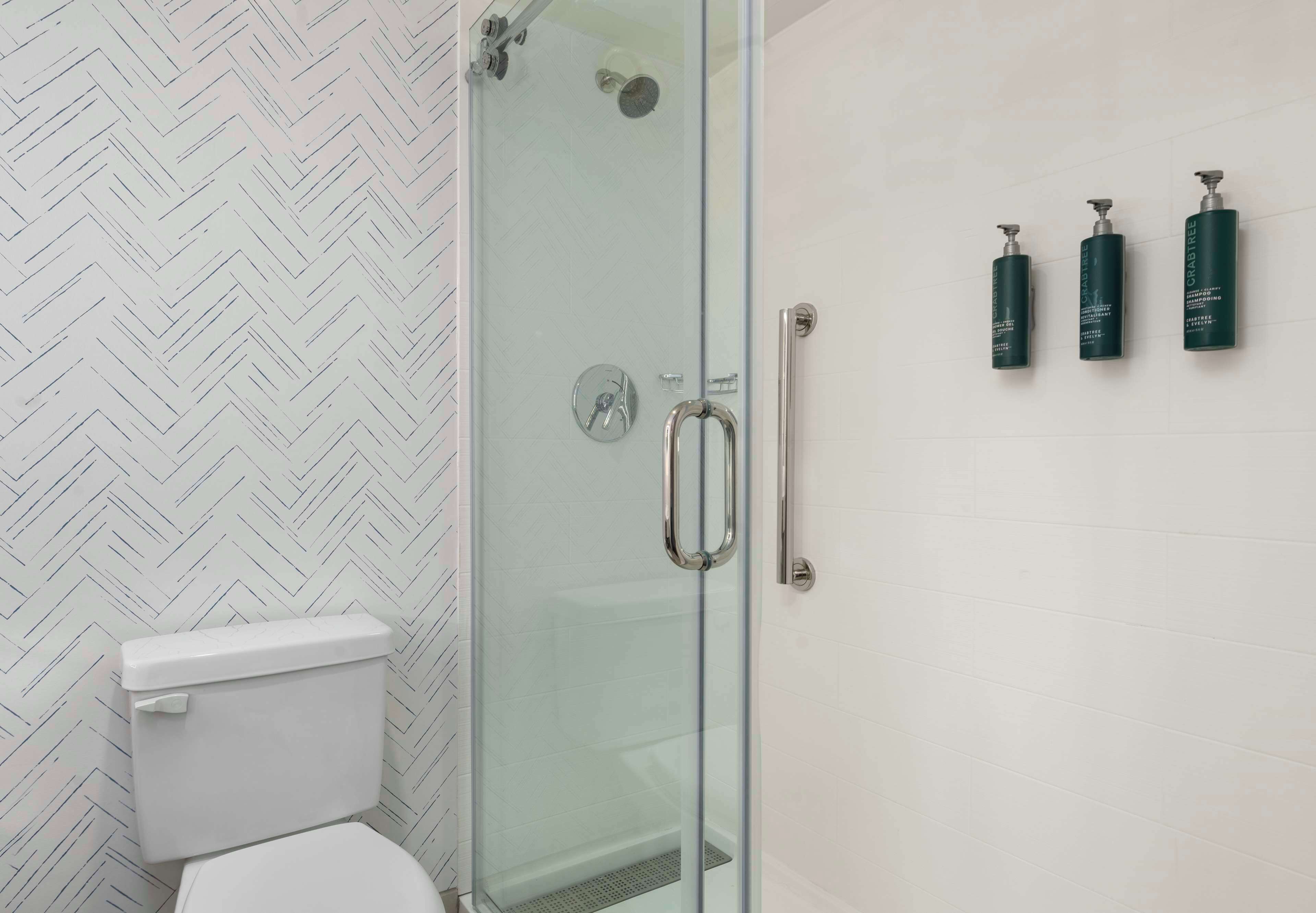Une salle de bain avec une douche à parois de verre, des toilettes et trois bouteilles vertes accrochées au mur.