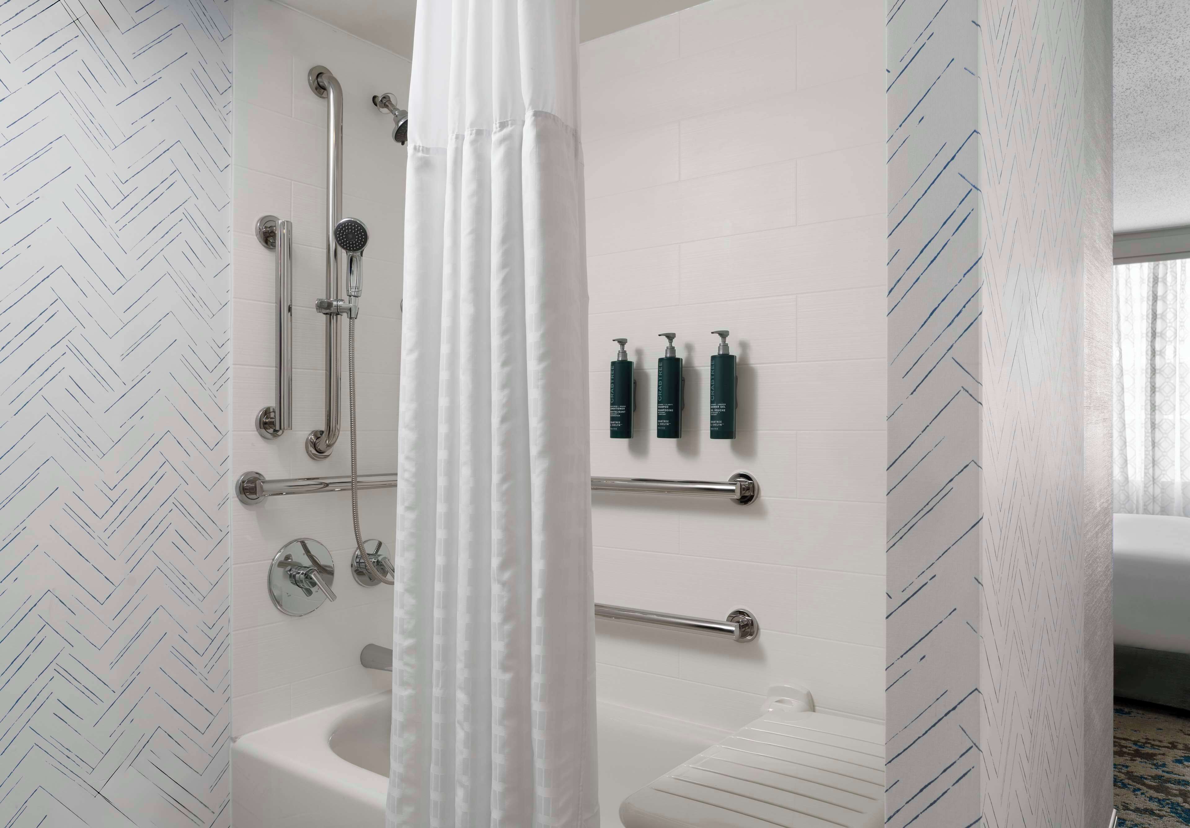 A modern bathroom with a shower, toilet, and bathtub. There are handrails and a towel rack.