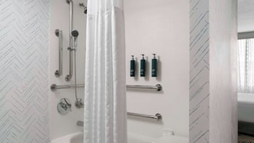 A modern bathroom with a shower, toilet, and bathtub. There are handrails and a towel rack.