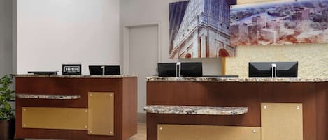 A hotel reception desk with a wooden finish and a digital screen displaying the hotel's name.