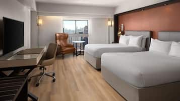 Une chambre d’hôtel équipée d’un bureau, de deux lits, d’une chaise, d’une petite table et offrant une vue sur la ville par la fenêtre.