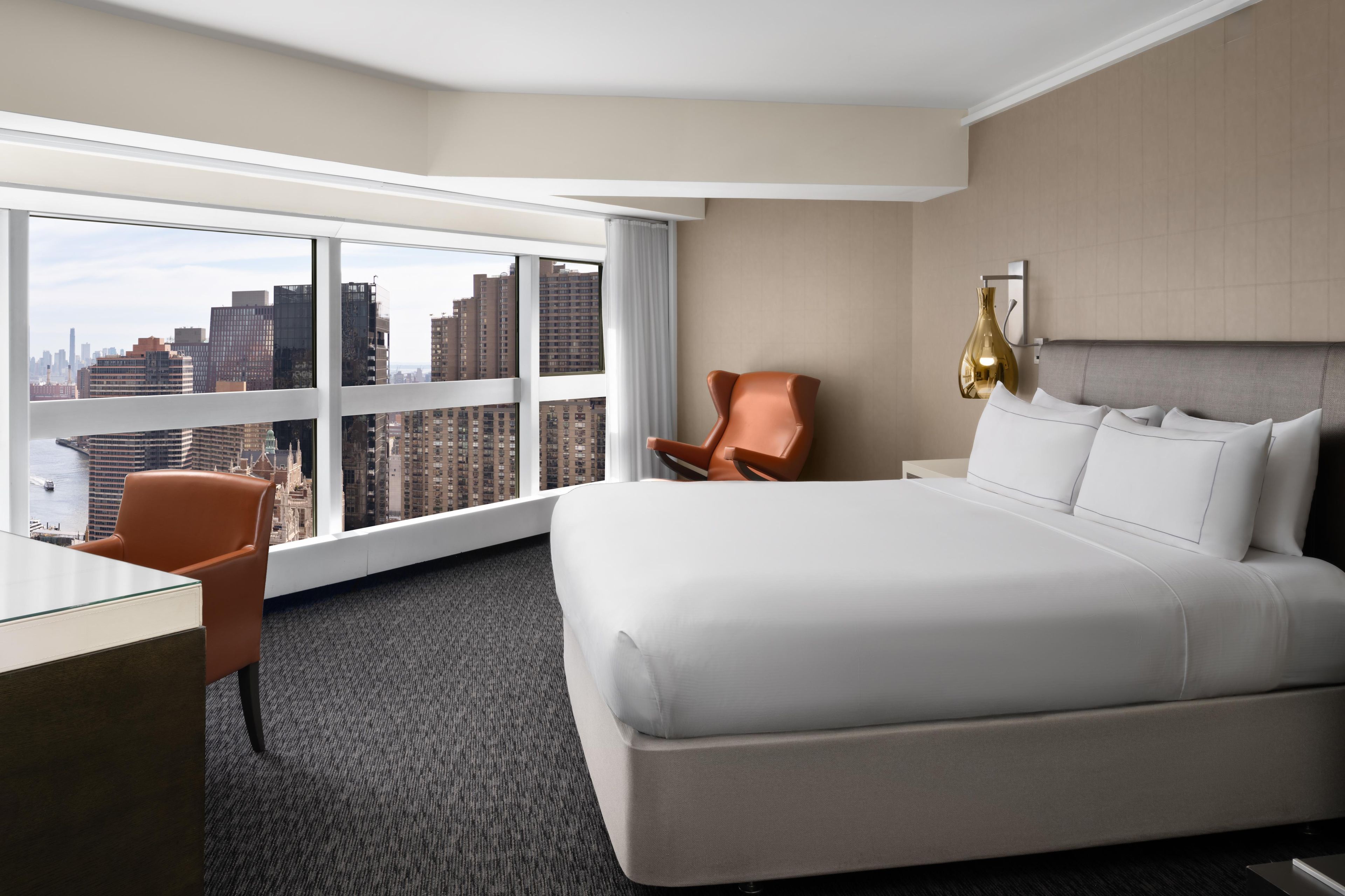 A hotel room with a large bed, a desk, a chair, and a view of the cityscape.