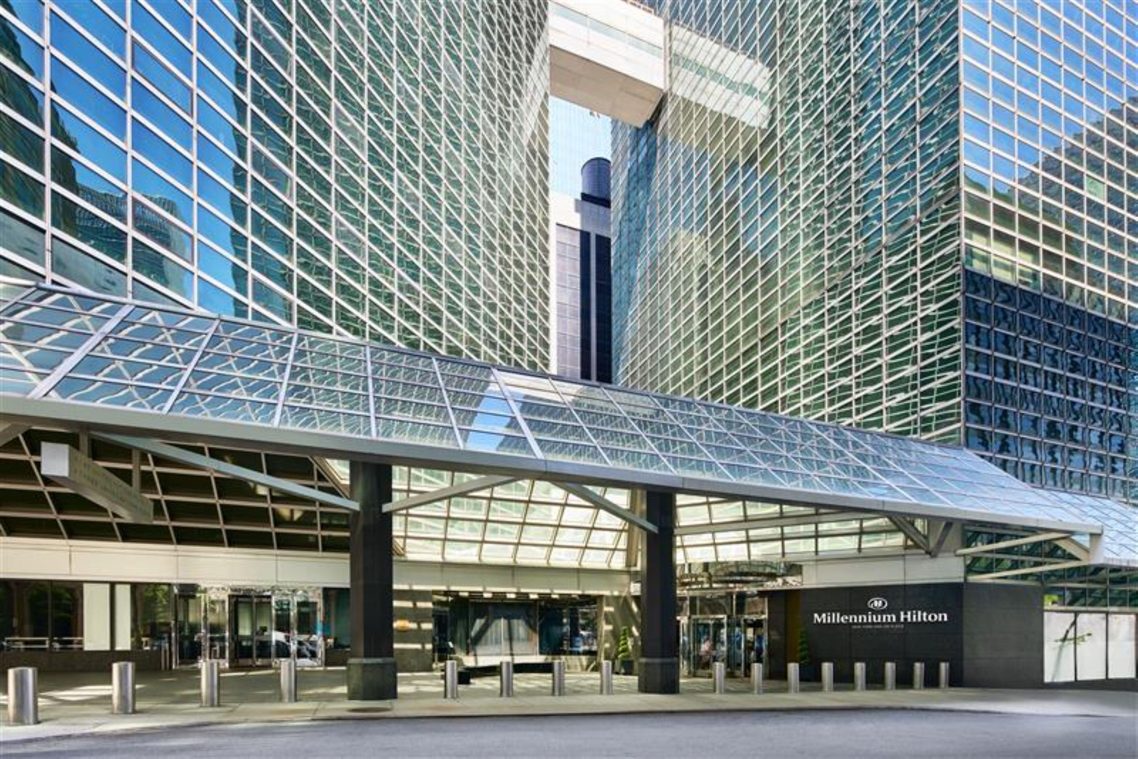 Una entrada de hotel moderna con un toldo de cristal y un llamativo letrero que dice 'Millennium Hilton'.
