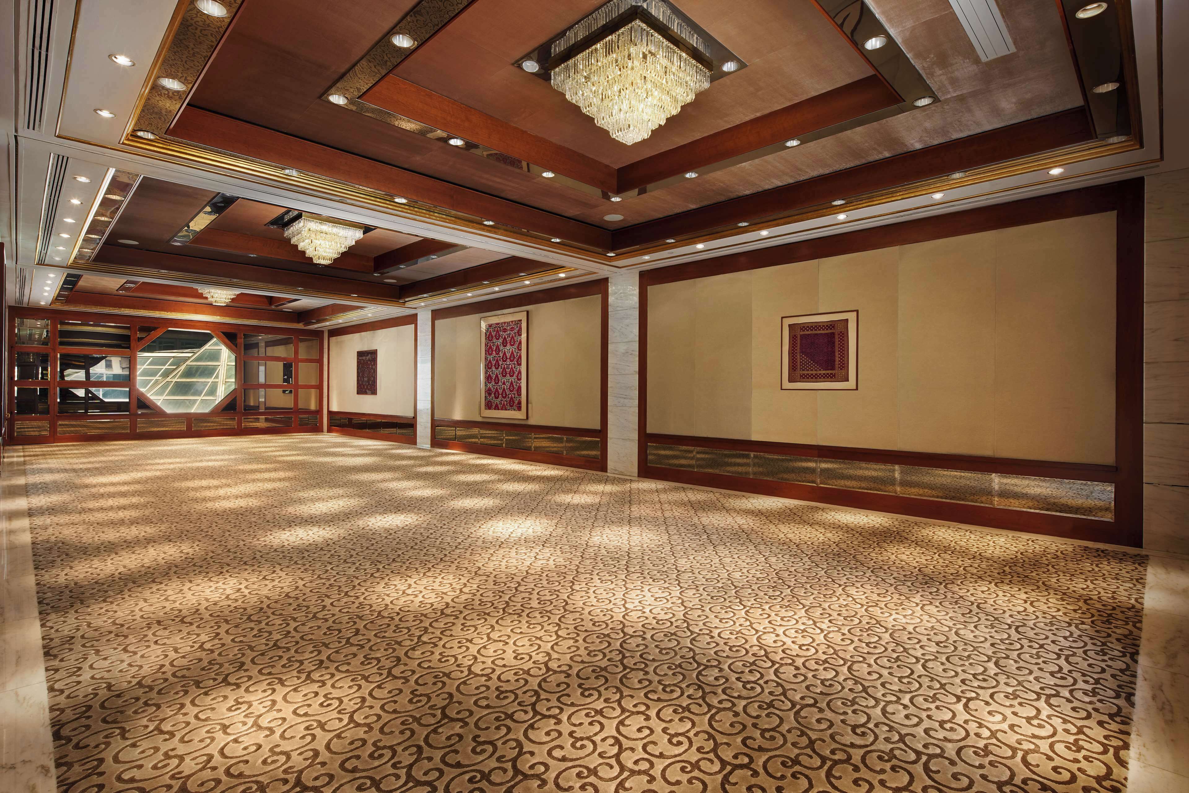 A spacious hall with patterned carpet, wooden paneling, and a large chandelier.