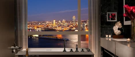 A bathroom with a large window overlooking a cityscape at night.