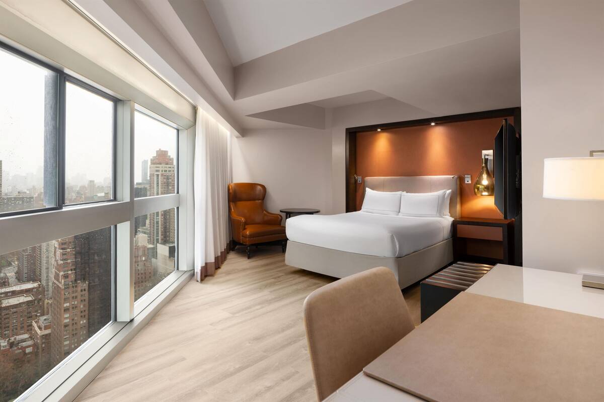 Une chambre d’hôtel moderne dotée d’une grande fenêtre, d’un lit, d’un bureau et d’une chaise.
