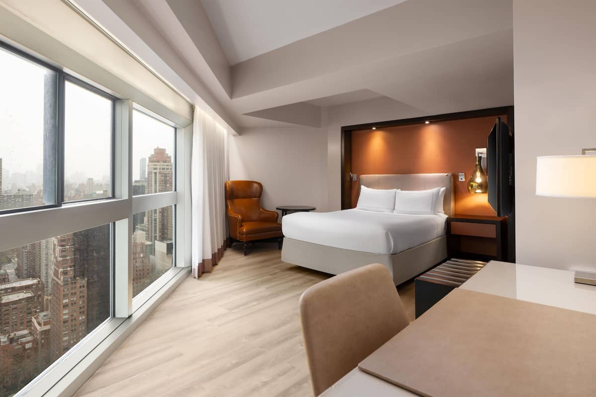Une chambre d’hôtel moderne dotée d’une grande fenêtre, d’un lit, d’un bureau et d’une chaise.