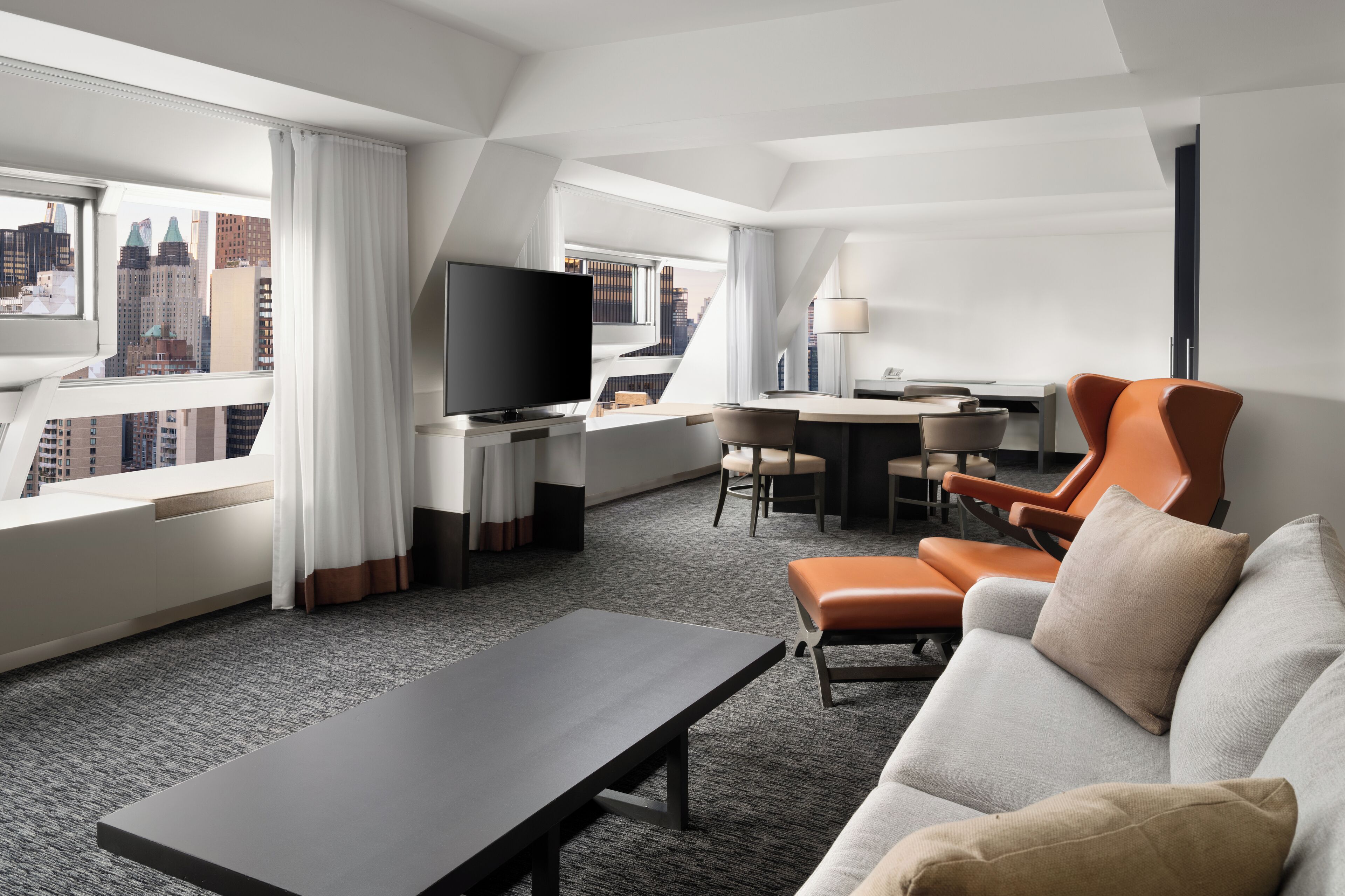 Una habitación de hotel moderna con vista a la ciudad, televisor de pantalla plana, sofá, mesa de comedor y escritorio.