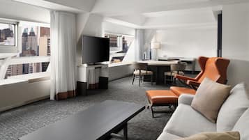 Una habitación de hotel moderna con vista a la ciudad, televisor de pantalla plana, sofá, mesa de comedor y escritorio.