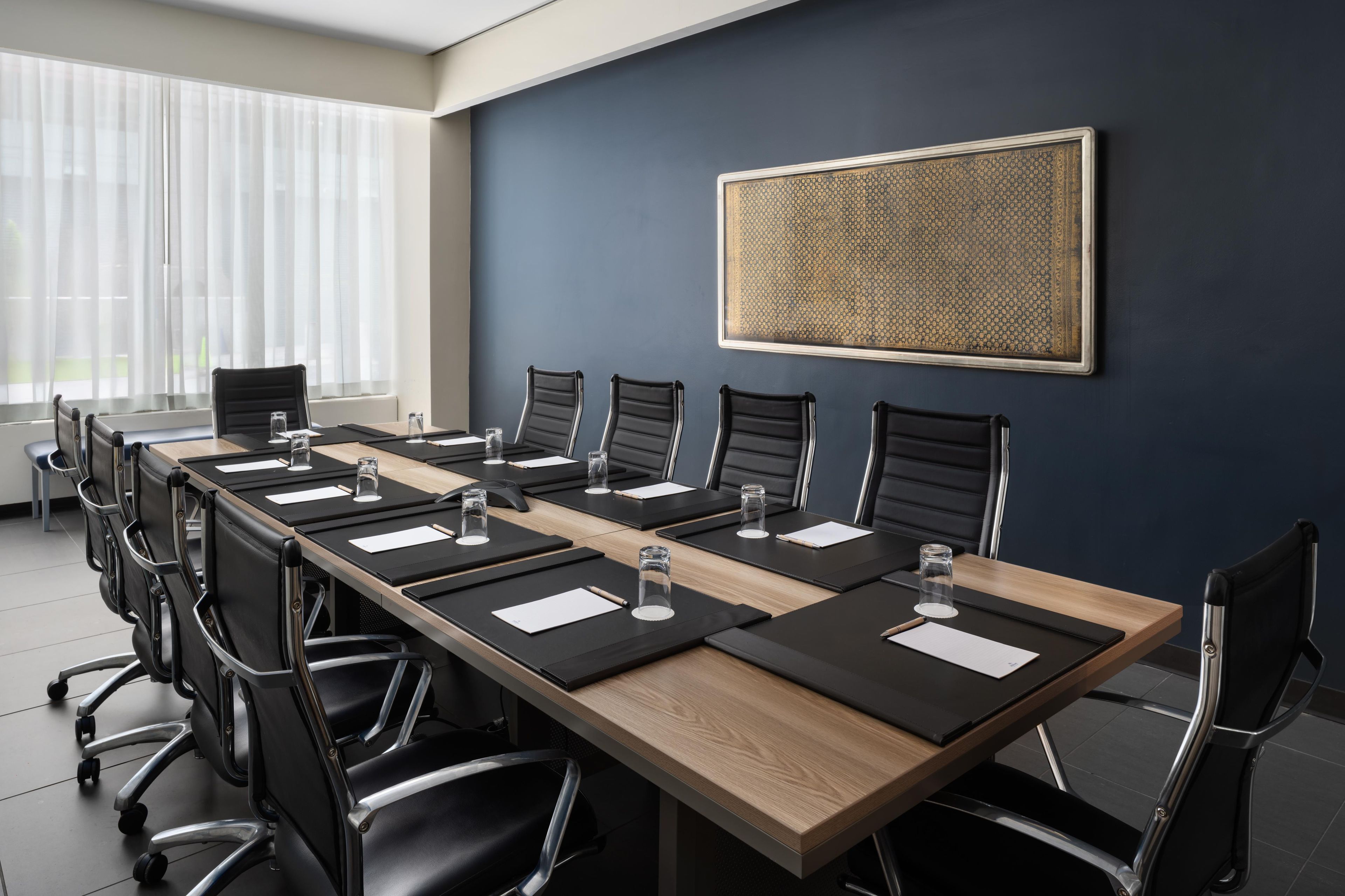A conference room with a long table, black chairs, and a large patterned artwork on the wall.